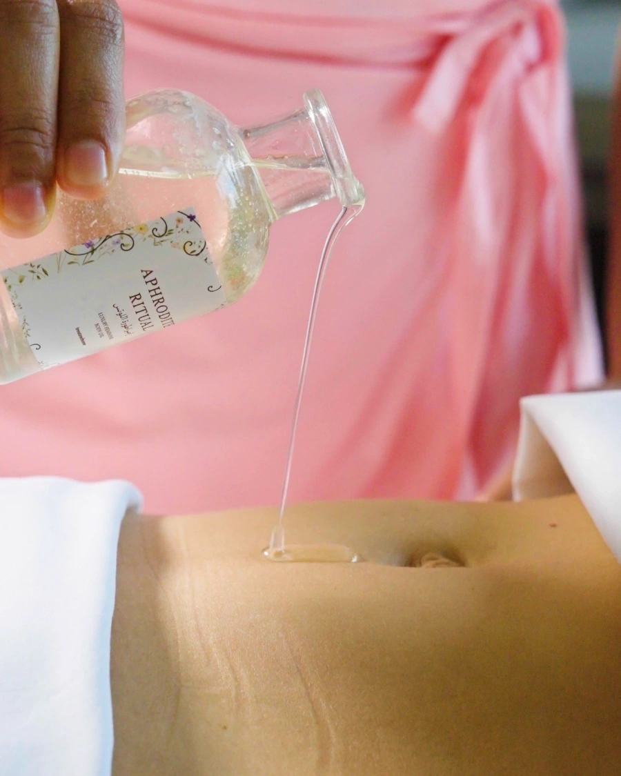 Aphrodite Ritual body oil being poured during a treatment, against a pink drape