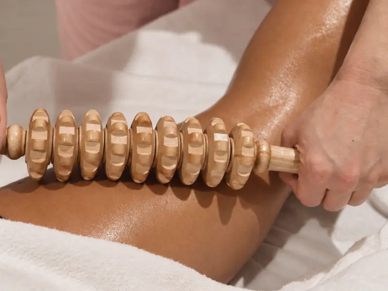 A wooden maderotherapy roller being worked along the thigh